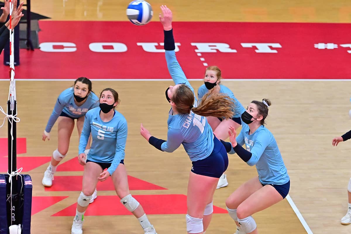 A group of young female adults make a play for a volleyball in the air